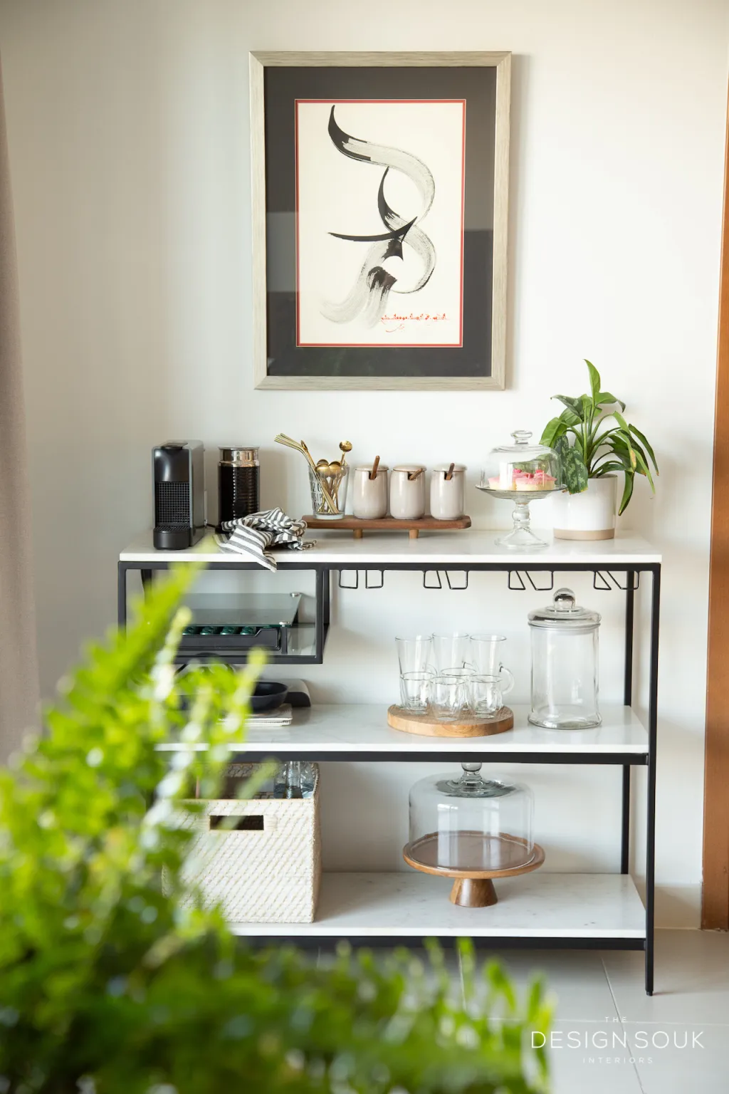 a corner of a office holds a tiered table with coffee bar items.