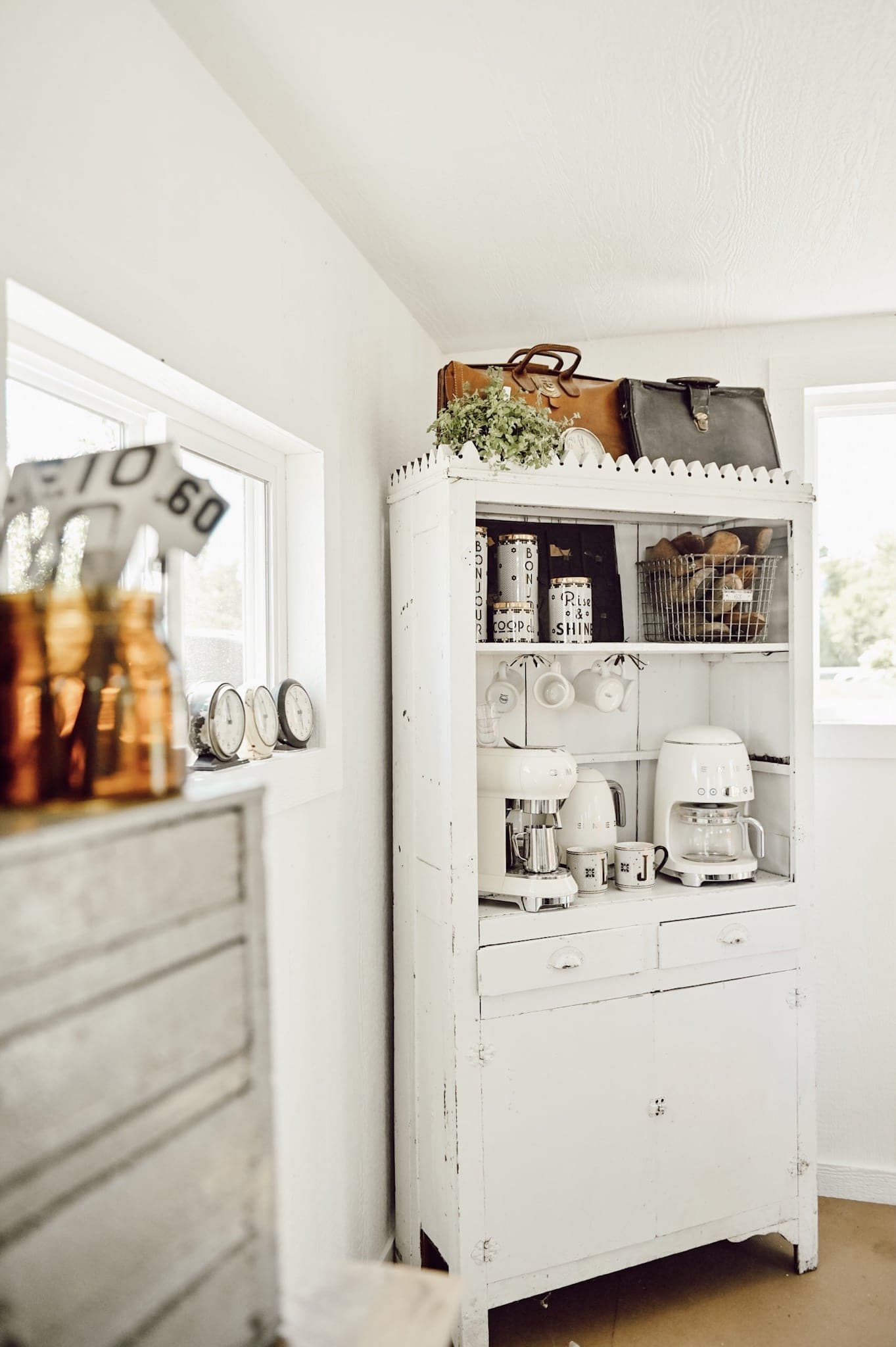 A rustic tall chippy white cabinet is used for a coffee station