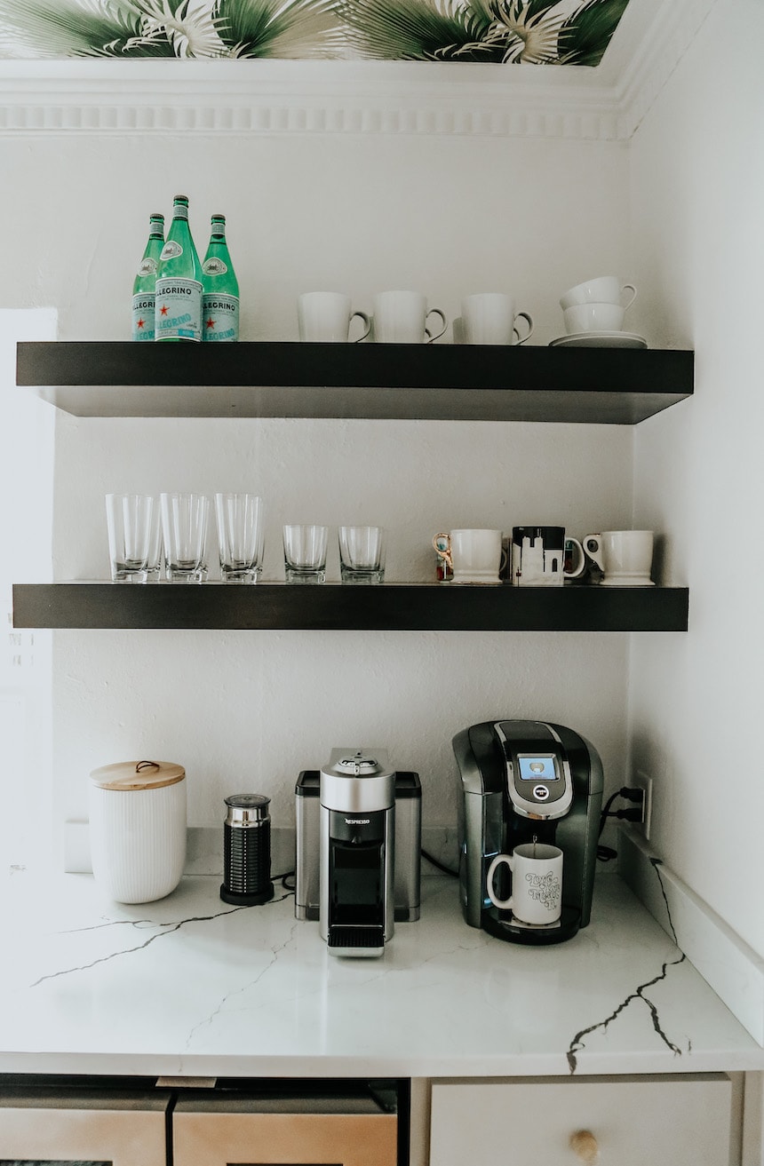 black floating shelves in a kitchen hold coffee mugs and coffee essentials for a coffee bar.
