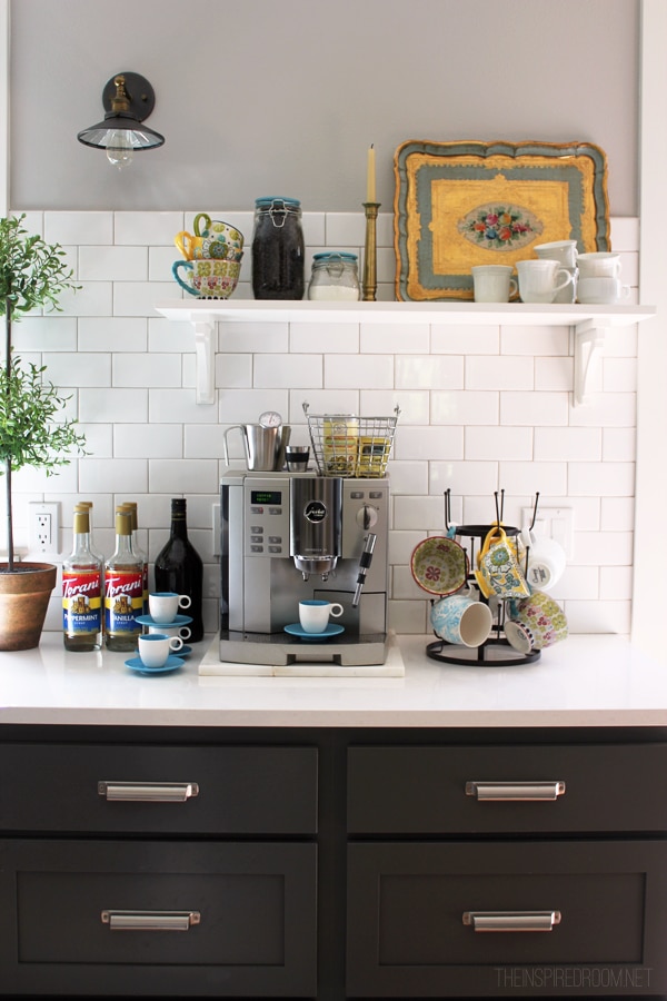 coffee station on a kitchen counter with a coffee mug tiered rack, syrups, and a floating shelf with more coffee mugs