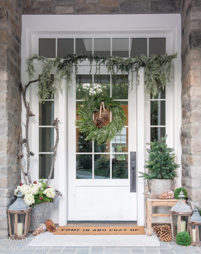 holiday front porch with evergreen wreath, pinecones, and lanterns