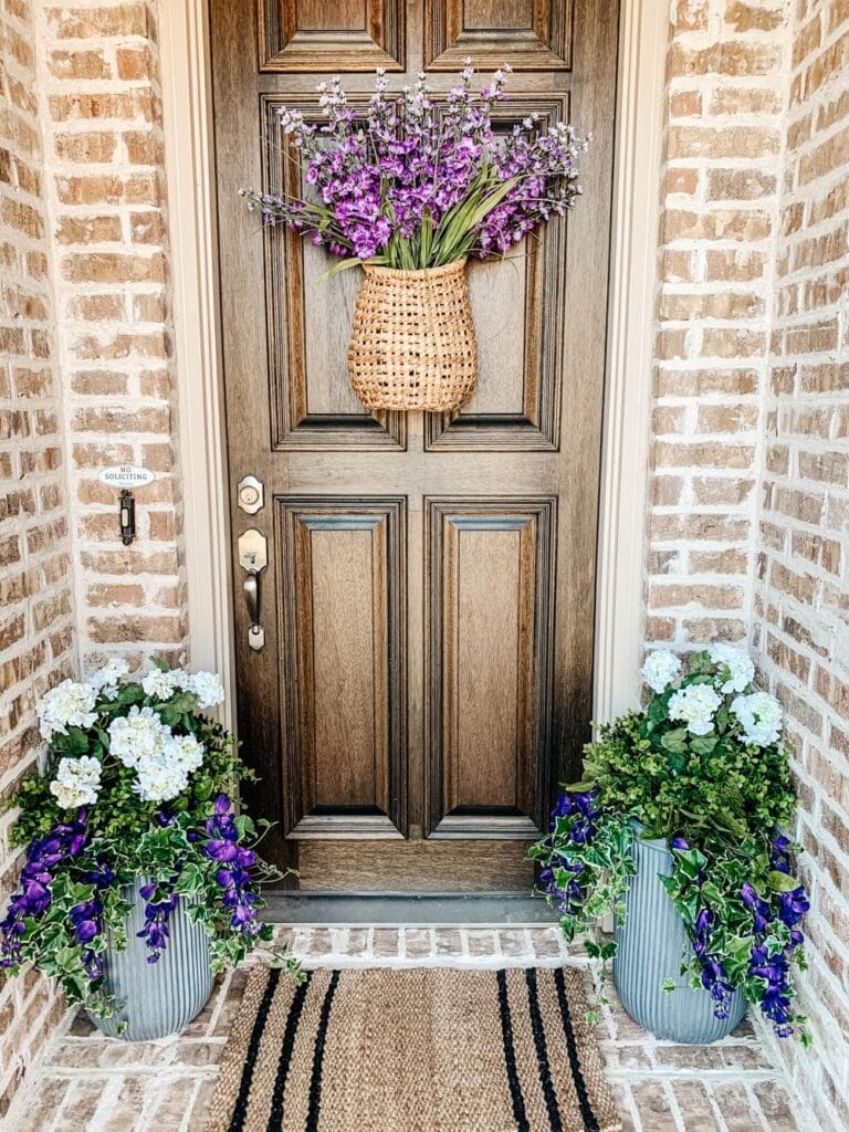 front porch with wood door with hanging basket with purple flowers