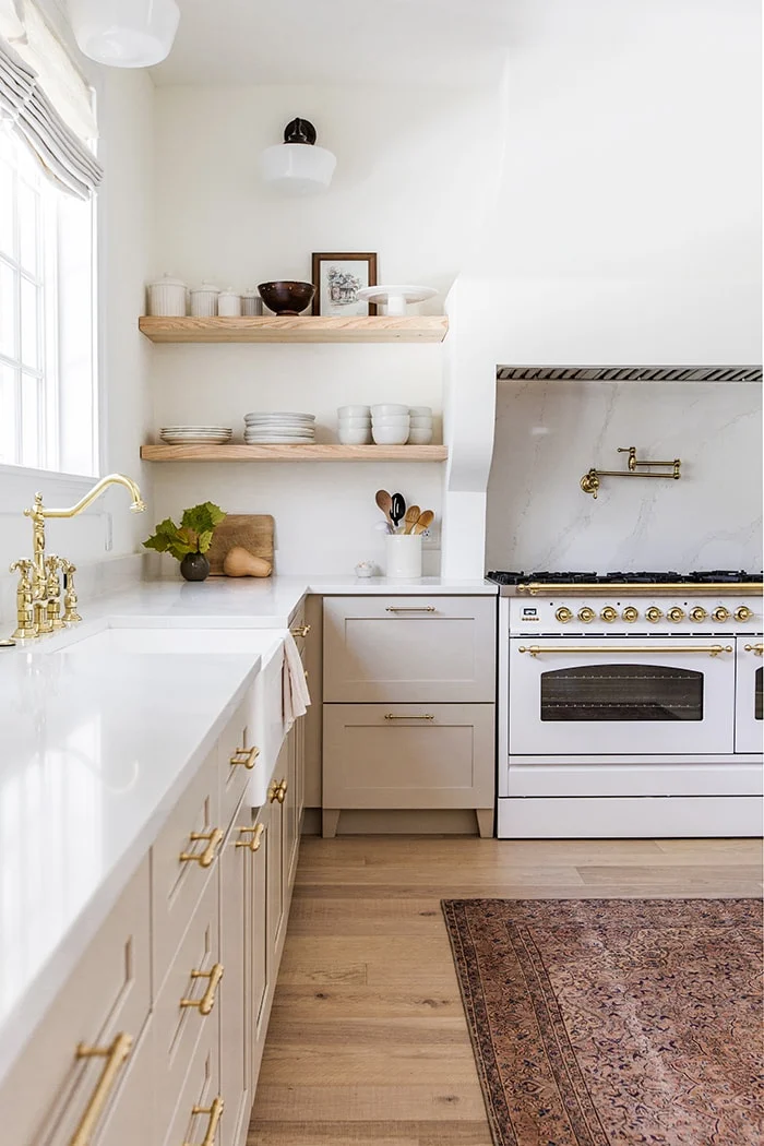wood floating shelves, beige kitchen cabinets, gold faucet, white range.