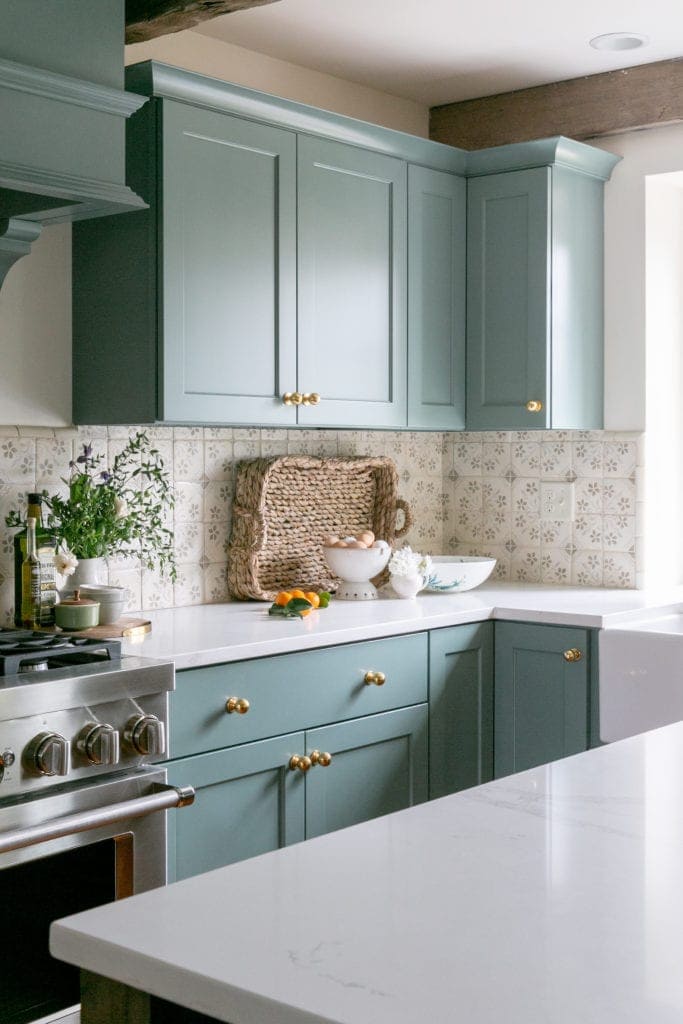 dark teal kitchen cabinets with a flower patterned tile for a backsplash and gold cabinet hardware