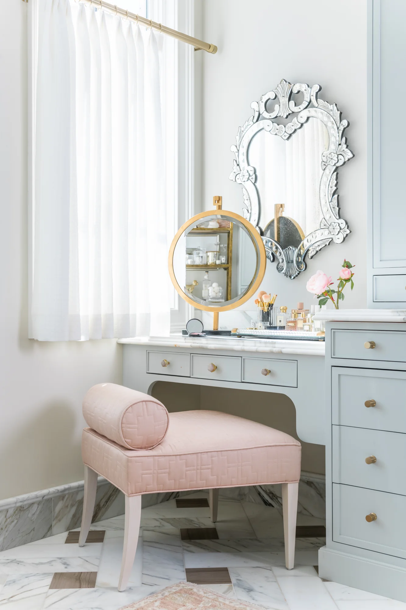 Blush vanity chair in a bathroom with light blue cabinets and gold hardware