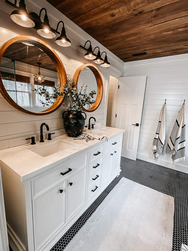 vintage style farmhouse bathroom with rustic wood ceiling, white cabinets, and black hardware