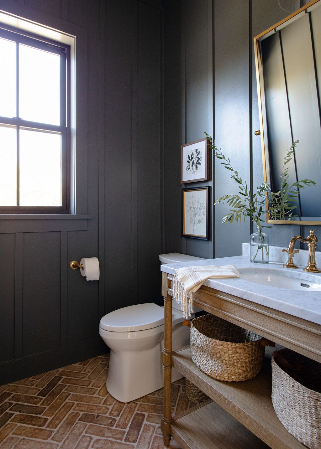 dark black wall paneling with a wood vanity cabinet and farmhouse style sink, gold faucet and mirror