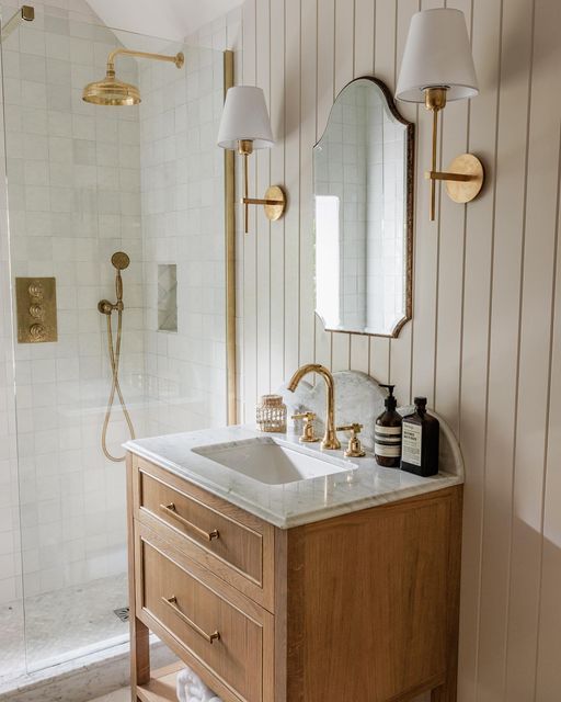 beige vertical shiplap walls with a wood vanity and gold sconces in a bathroom