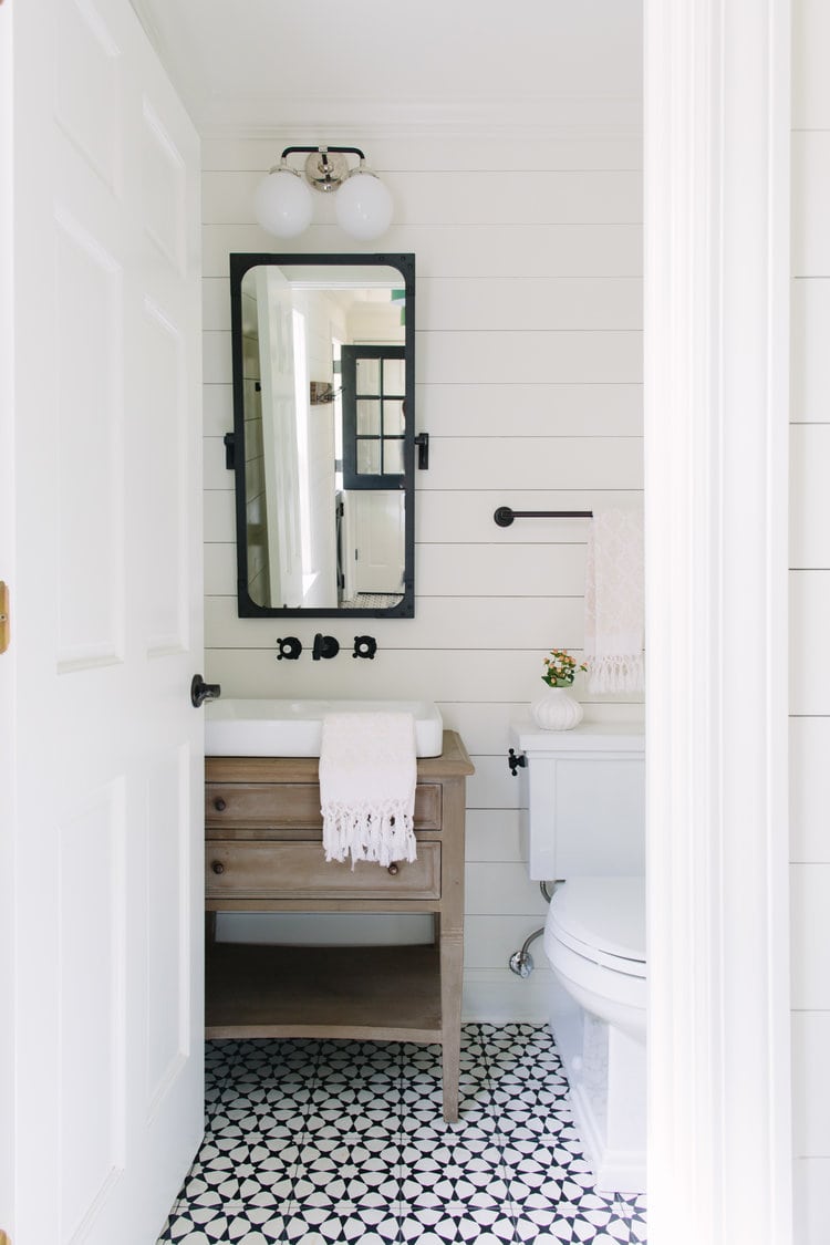 black and white patterned tile floor with a wood vanity, black hardware in this farmhouse bathroom.