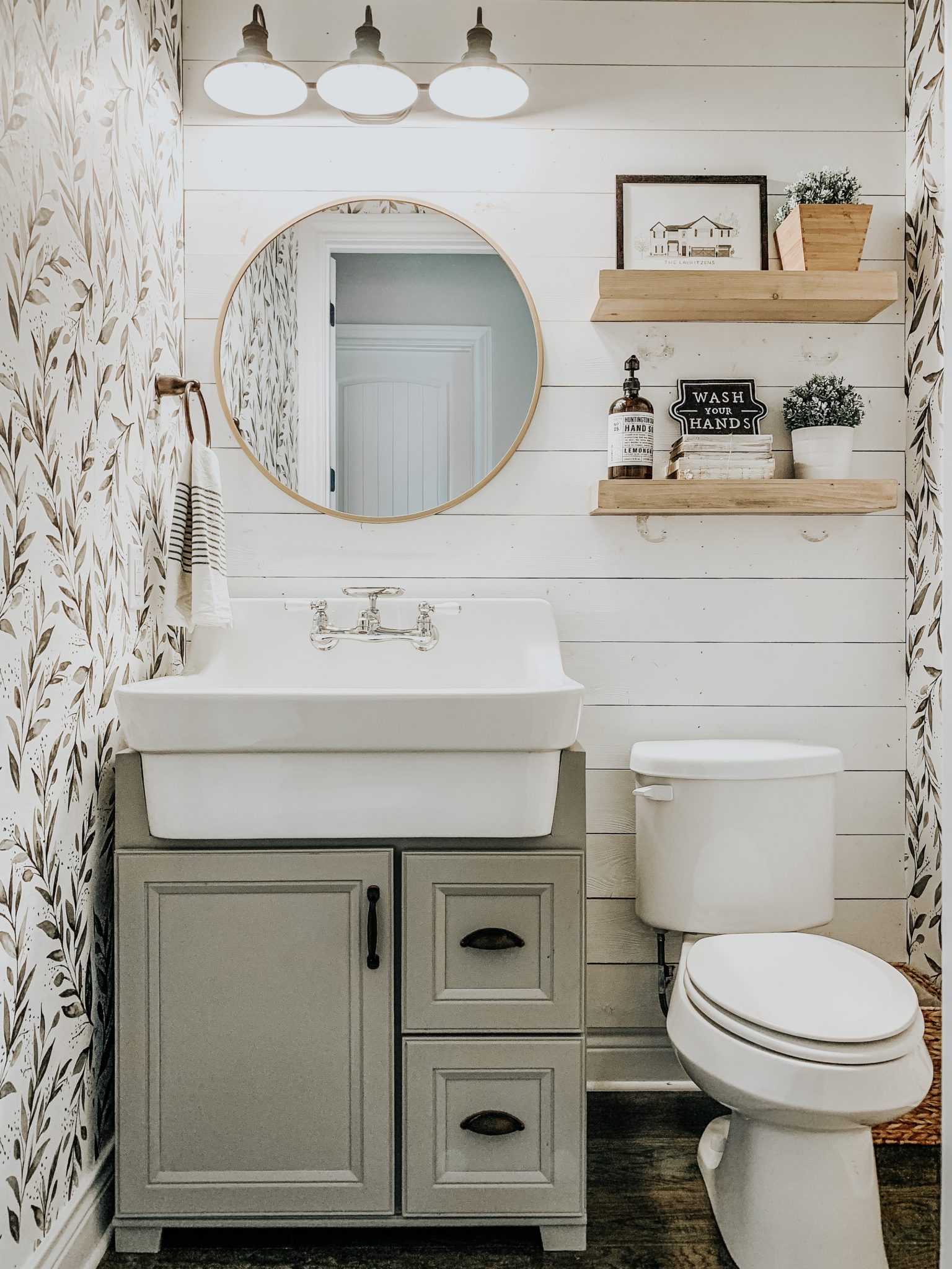 sage green cabinet with a vintage sink and leaf print wallpaper in this farmhouse bathroom
