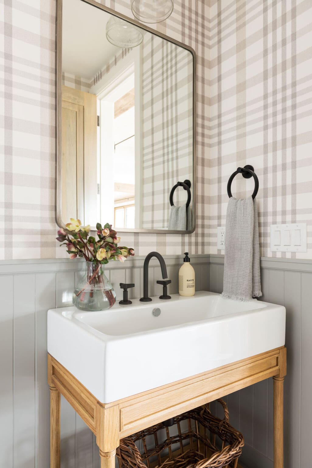plaid wallpaper, vertical shiplap walls painted a taupe color, black hardware in this farmhouse powder room.