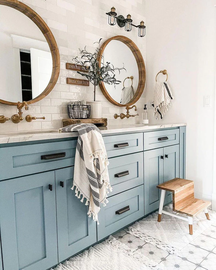 light blue cabinets with black hardware and gold faucets in a rustic farmhouse bathroom