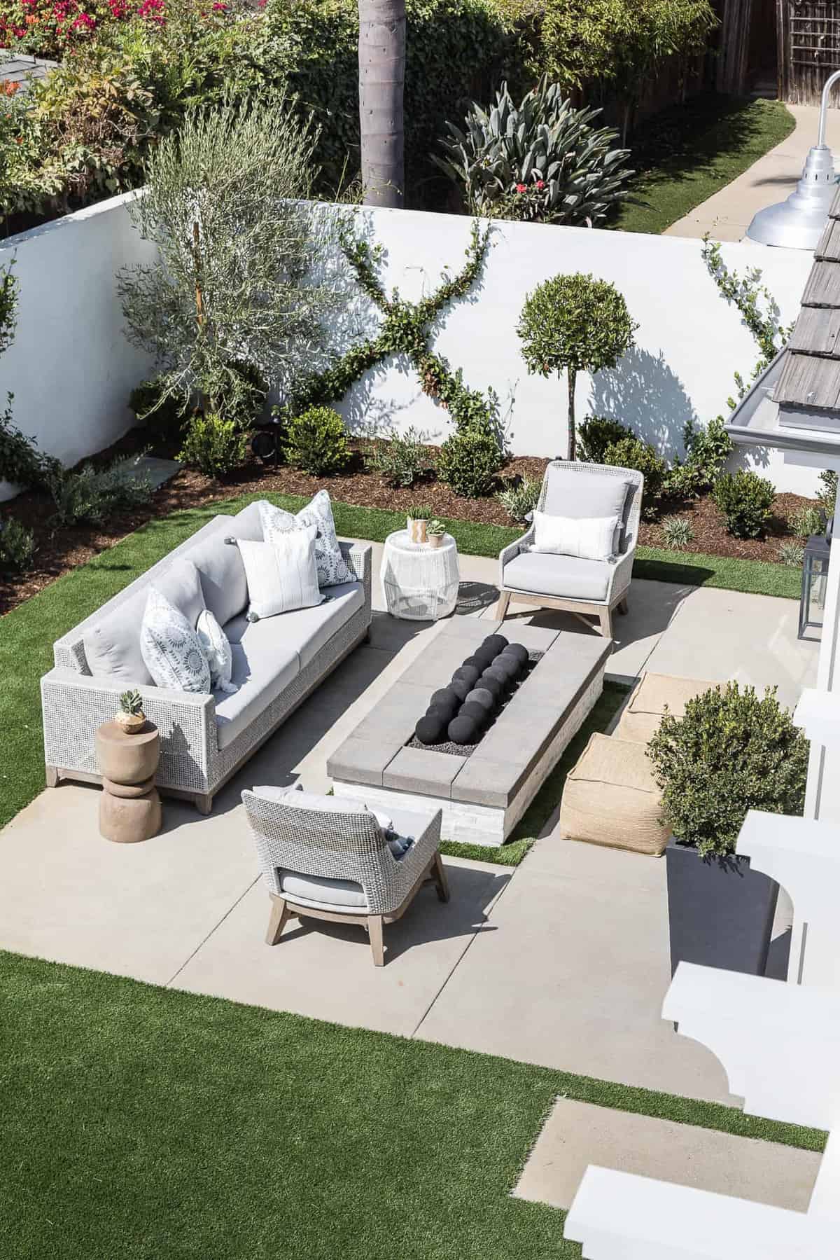seating area outside on a patio with a sofa, 2 chairs and a table made from a rectangular fire pit