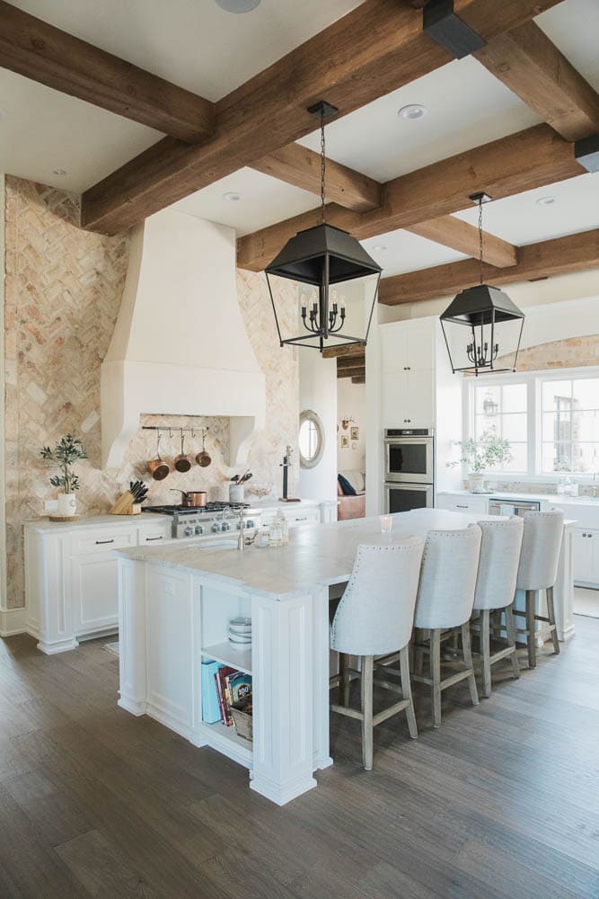 white kitchen with rustic wood beams, black French lanterns above island, upholstered barstools