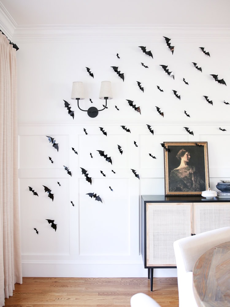 Black paper bats flying up a dining room wall above a sideboard